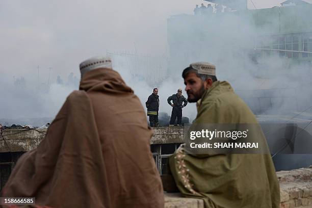 Afghan shopkeepers look on as firefighters work over the remains of shops after a huge fire swept through a market in Kabul on December 23, 2012. A...