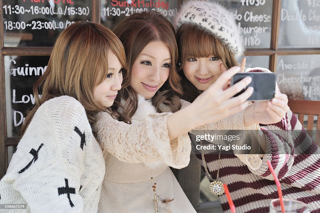 Three young women are taking photo on smartphone