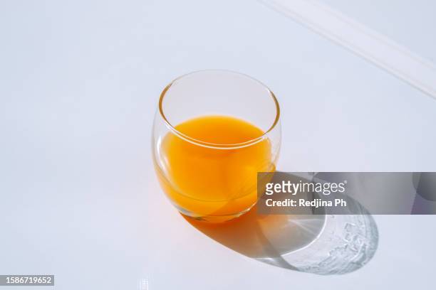 glass of freshly squeezed orange juice on a plain white background, with a vibrant sunlit shadow on a hot summer day - orange juice glass white background stock pictures, royalty-free photos & images