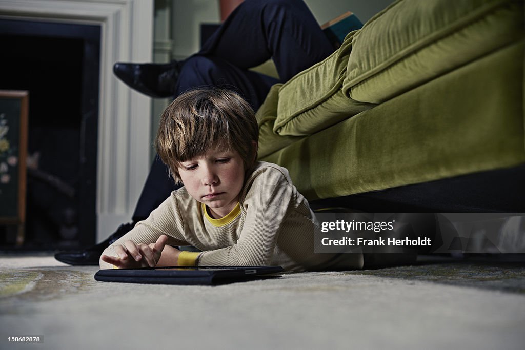 Boy on tablet computer under sofa