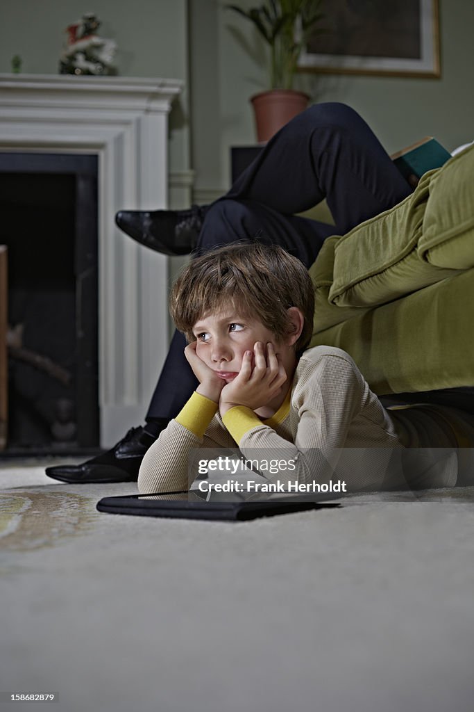 Bored looking boy using tablet computer under sofa