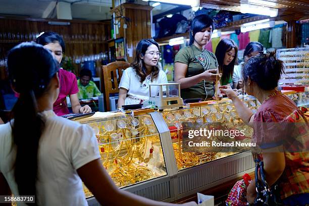 At a shopping center in Mawlamyine, women looking at and choosing gold ornaments while chatting with the several shop-keepers of the gold shop..