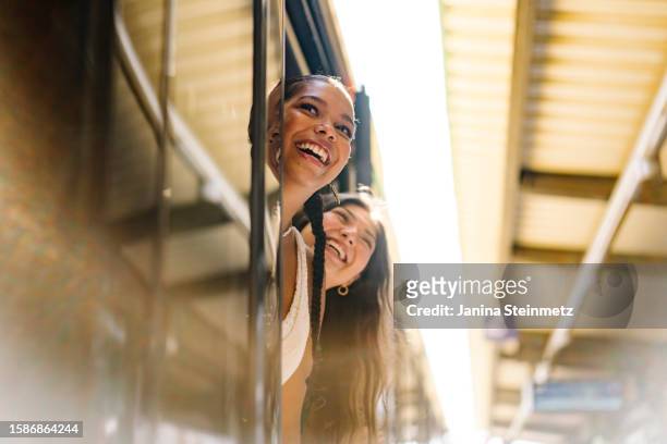 portrait shot of two young women looking out of an open door of a train on a platform and smiling - travel stock-fotos und bilder