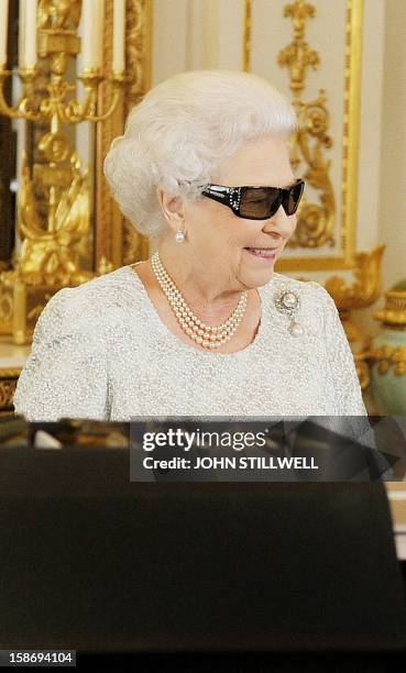 In this picture taken on December 7, 2012 Queen Elizabeth II wears 3D glasses to watch th recording of her Christmas message to the Commonwealth...
