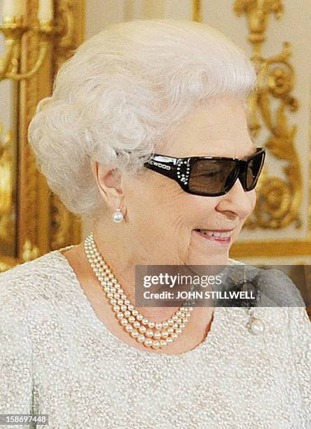 In this picture taken on December 7, 2012 Britain's Queen Elizabeth II wears 3D glasses to watch the recording of her Christmas message to the...