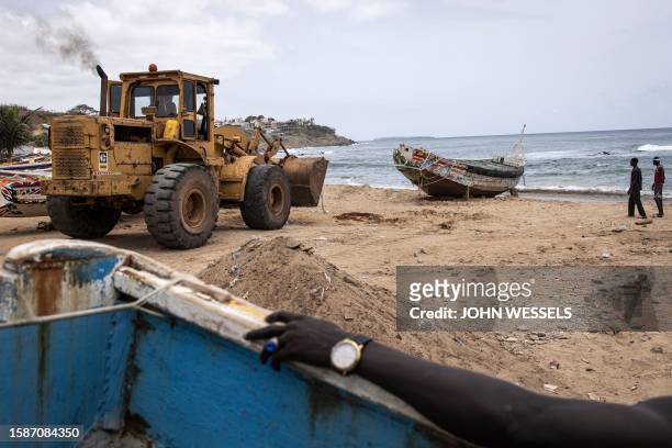 Fishermen look on as a bulldozer tries to move a beach pirogue in Dakar on August 9 in which 17 migrants lost their lives after it capsized off the...