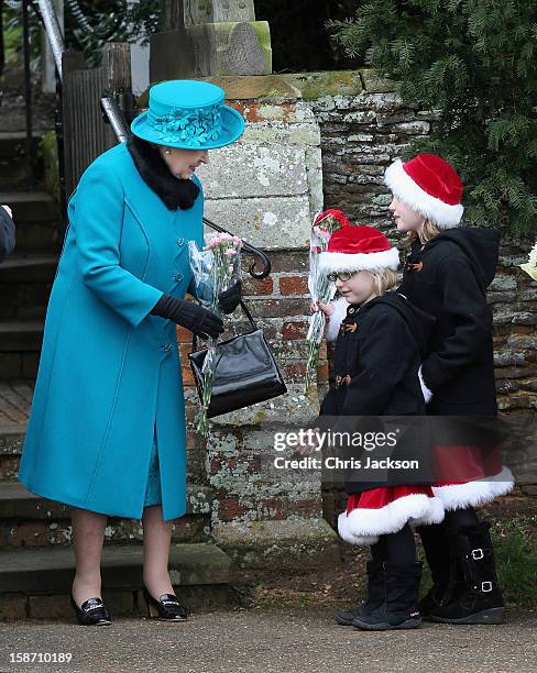 Queen Elizabeth II is presented with flowers by two girls wearing Santa outfits as she leaves St Mary Magdalene Church after attending the...