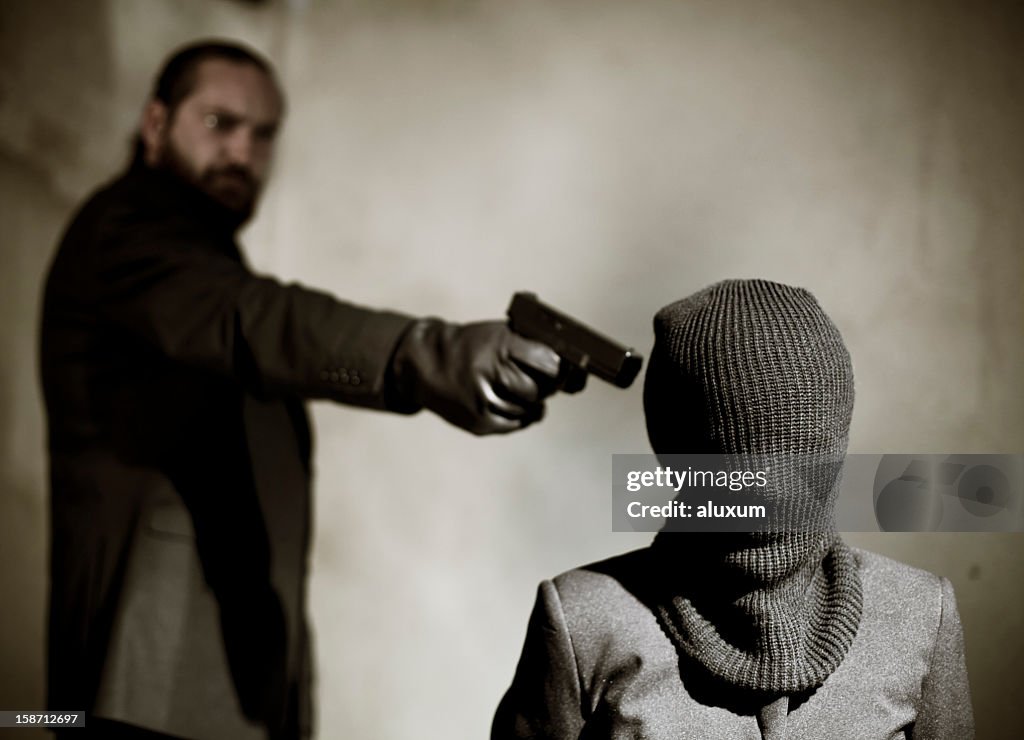 Bearded man pointing a gun at a man's temple to execute him