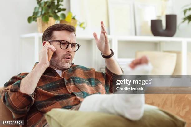 angry mature man with broken leg at home - human foot prints stock pictures, royalty-free photos & images