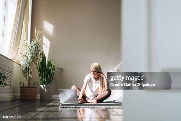 young woman student with long blonde hair working with laptop sitting on floor at home - studentenwohnung stock-fotos und bilder