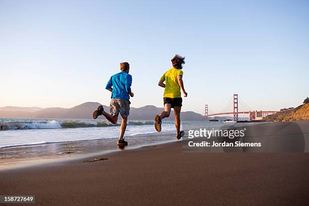 two men running during sunset. - baker beach stock pictures, royalty-free photos & images
