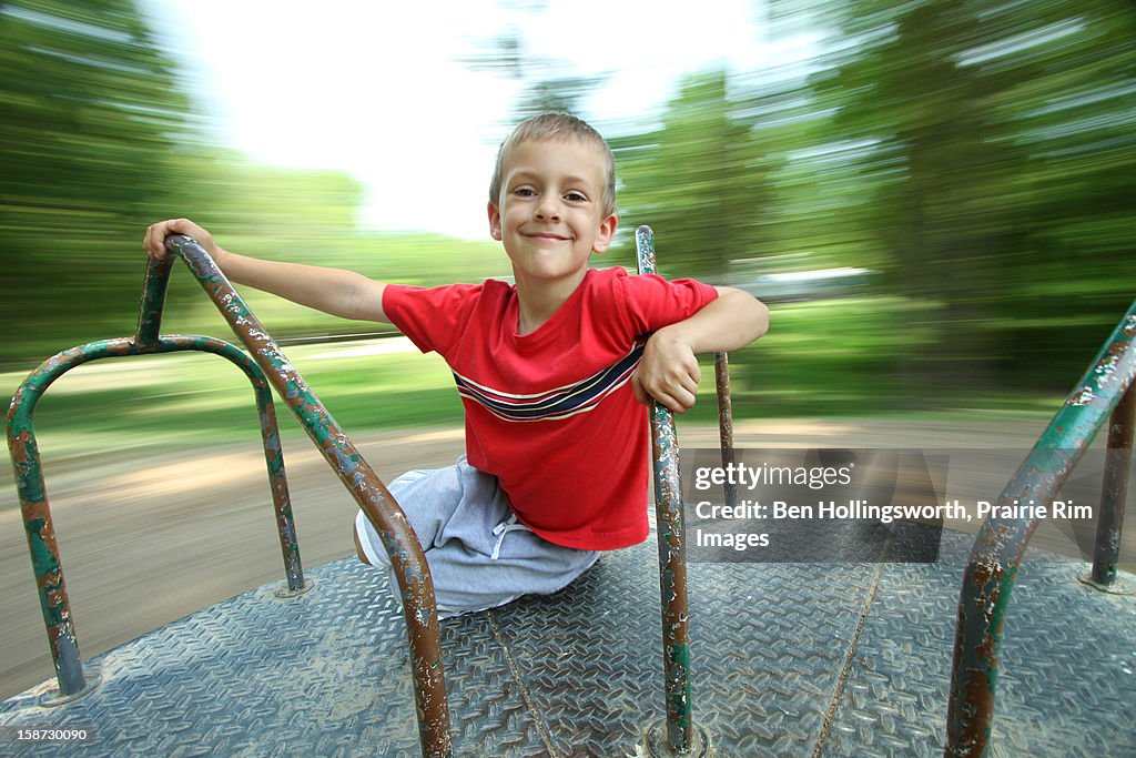 Boy spinning on playground merry-go-round