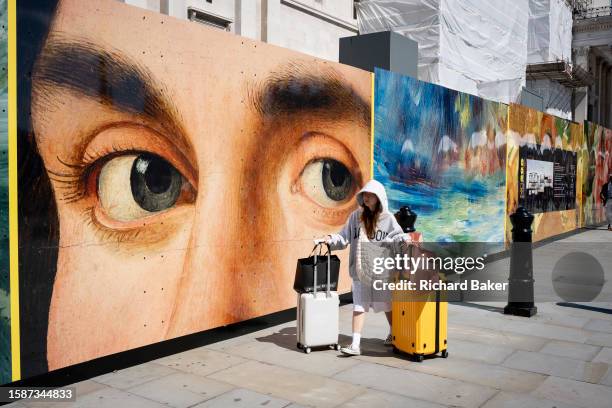 The eyes from a detail of Antonello da Messina's 'Portrait of a Man' look to a tourist who wheels her baggage past the National gallery in Trafalgar...