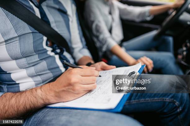 young driving instructor grading his female student using a checklist - rijbewijs stockfoto's en -beelden