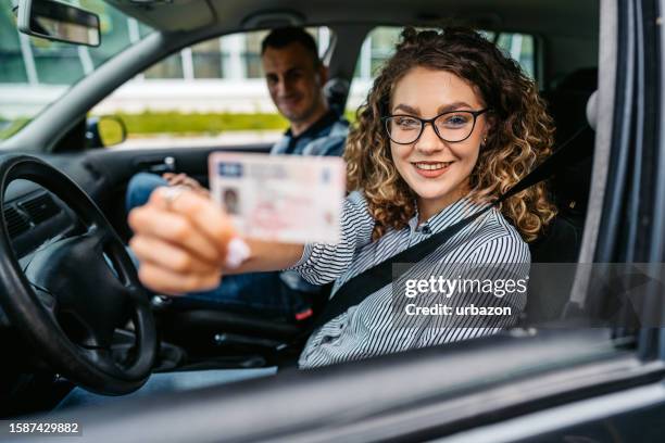 une jeune étudiante tenant son nouveau permis de conduire dans la voiture - carte d'identité photos et images de collection