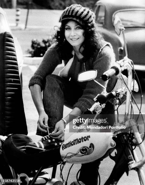 Italian actress and singer Maria Grazia Buccella lacing up her shoes putting her leg on the saddle of a motorcycle. Rome, 1970s