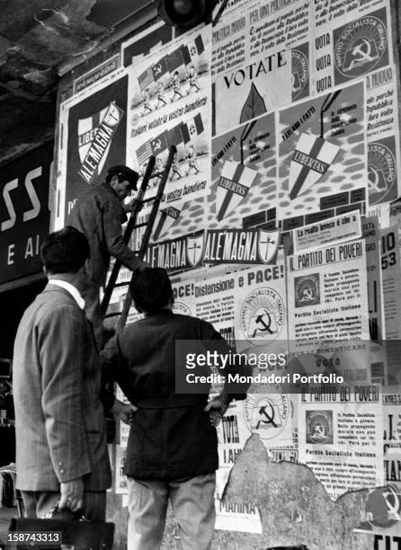 Some men observing the electoral posters of Christian Democratic Party and Italian Socialist Party . Italy, 1953