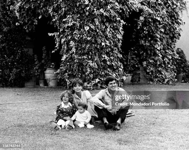 Gianni Morandi with his wife, the actress Laura Efrikian and their children and their children Marianna and Marco, sitting in the garden. Rome, 1974.