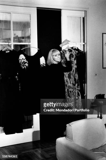Italian actress and singer Carmen Villani arranging some dresses. Milan, 1970s