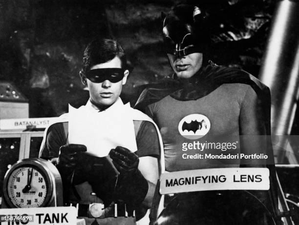 American actors Adam West and Burt Ward wearing the costumes of the comics superheroes Batman and Robin and reading a paper in the TV serie Batman....