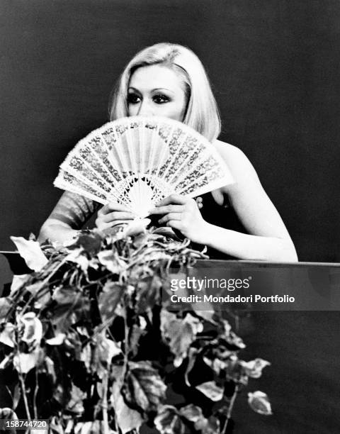 Dancer and presenter Raffaella Carrà in a dress showing her shoulders and a fan covering part of her face during the rehearsal of the TV show...