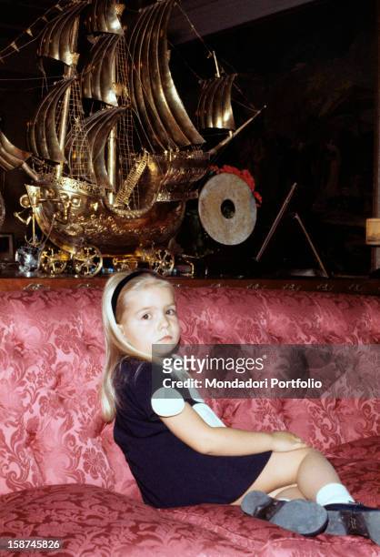 The little Infanta Elena, daughter of the princes of Spain Juan Carlos and Sophia, seats peaceably on a purple velvet sofa, next to a big gilted...