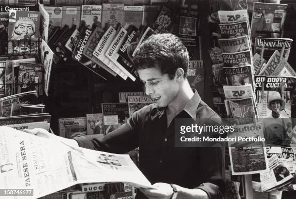 Italian actor Gabriele Lavia reading the newspaper Paese Sera. Rome, 1970s