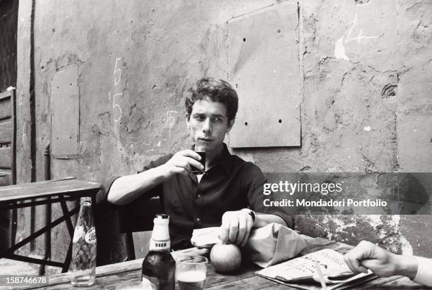 Italian actor Gabriele Lavia sitting at the table and drinking. Rome, 1970s