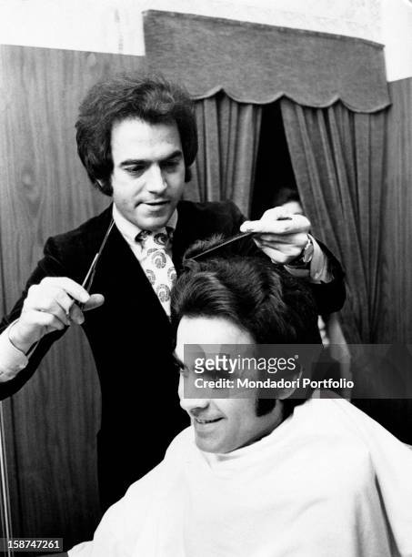 The Italian singer Mario Tessuto having his brother Renato's hair cut. Milan, 1970