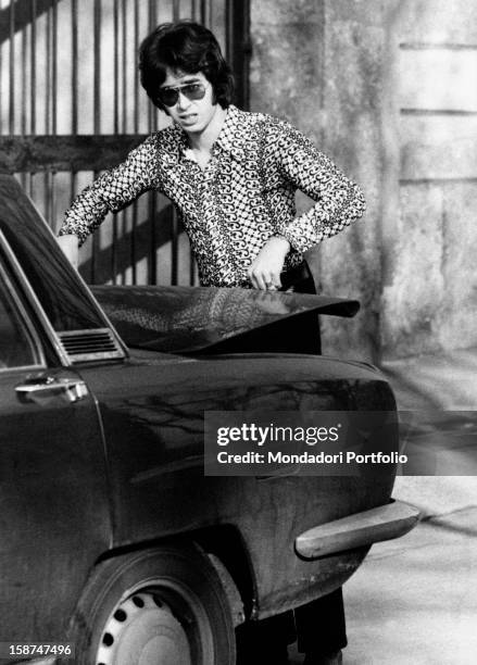 Italian musician and member of the band New Dada Franco Jadanza closing the boot of an Alfa Romeo car. Milan, 1970