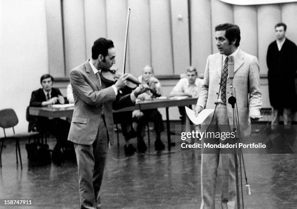 Italian TV host Corrado introducing a guest with a violin during a radio show. Rome, 1970s