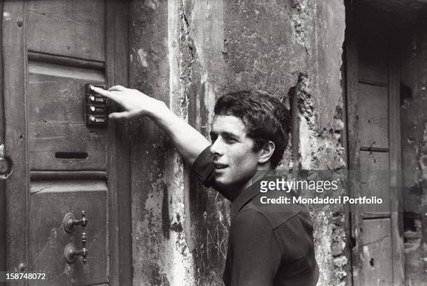 Italian actor Gabriele Lavia calling on the entryphone of a door. Rome, 1970s