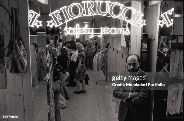 Italian fashion designer and entrepreneur Elio Fiorucci at the entrance of his shop in San Babila square. Behind him, the neon sign saying Fiorucci...