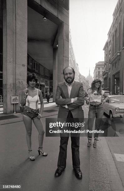 Italian fashion designer and entrepreneur Elio Fiorucci posing with two models wearing cloths designed by him. Milan, 1974