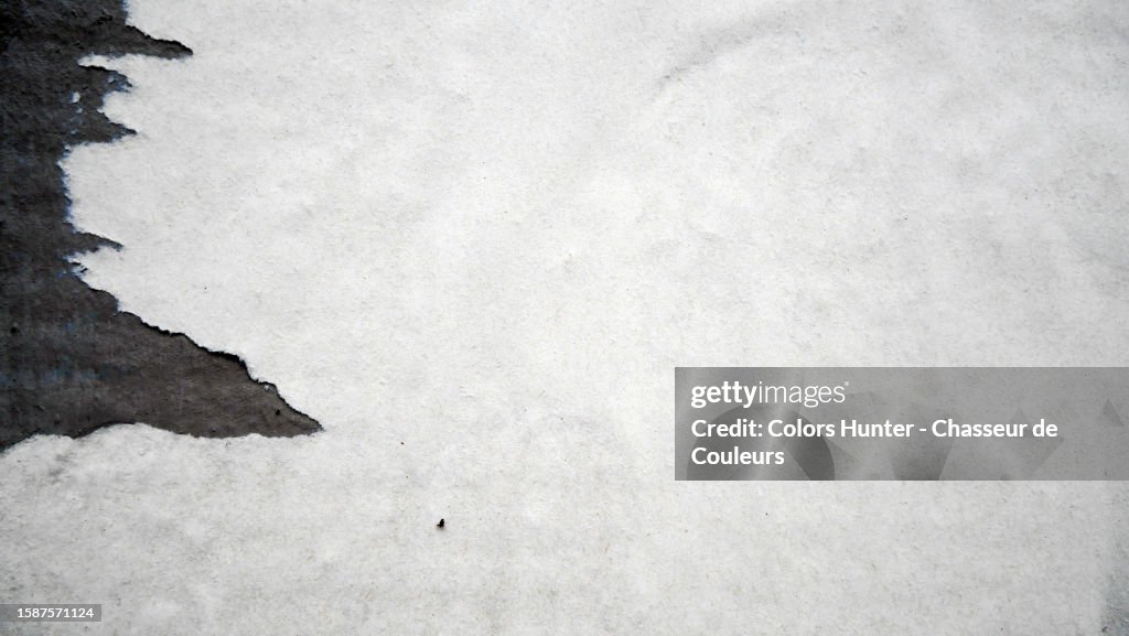 Close-up of a white poster pasted and torn on a black concrete wall in Paris, France