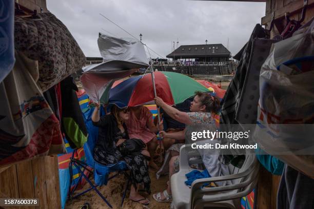 Friends shelter from the rain outside their beach hut on August 02, 2023 in Broadstairs, United Kingdom. August 2023 in the UK has seen erratic...