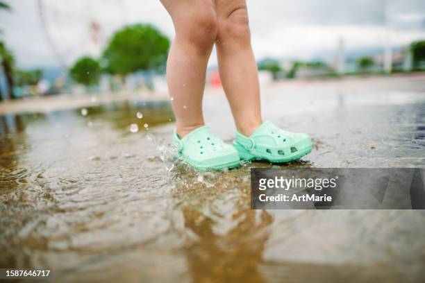 little girl playing with puddles and splashing water in a park in summer after rain - crocodile stock pictures, royalty-free photos & images