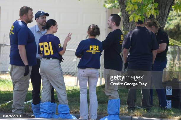 Officials and other law enforcement officers stand outside the home of Craig Robertson who was shot and killed by the FBI in a raid on his home this...