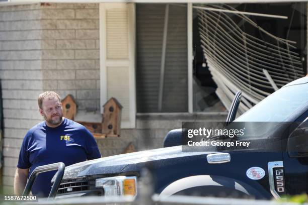 With a broken window in the background a FBI agent leaves the home of Craig Robertson who was shot and killed by the FBI in a raid on his home this...