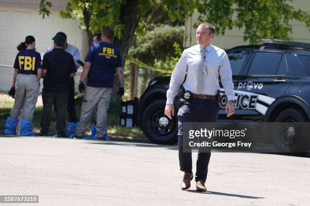 Provo police officer walks away as FBI officials and other law enforcement officers stand outside the home of Craig Robertson who was shot and killed...