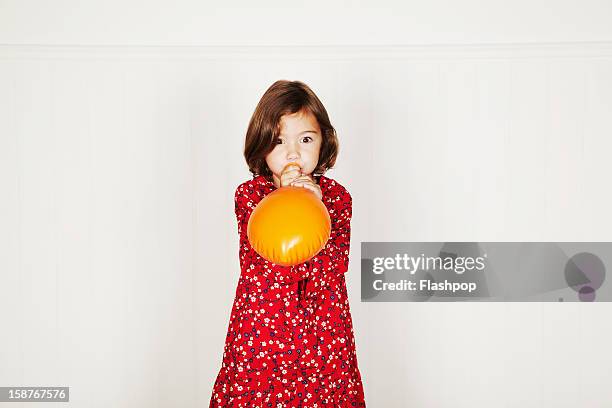 portrait of girl blowing up balloon - orange dress stock pictures, royalty-free photos & images