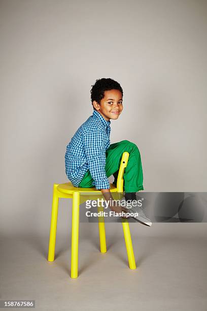 portrait of boy with chair pulling funny faces - green pants stock-fotos und bilder