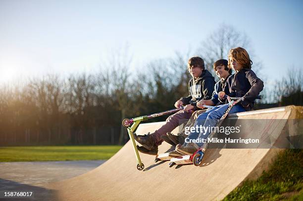 boys holding micro scooters sitting on ramp. - skatepark imagens e fotografias de stock