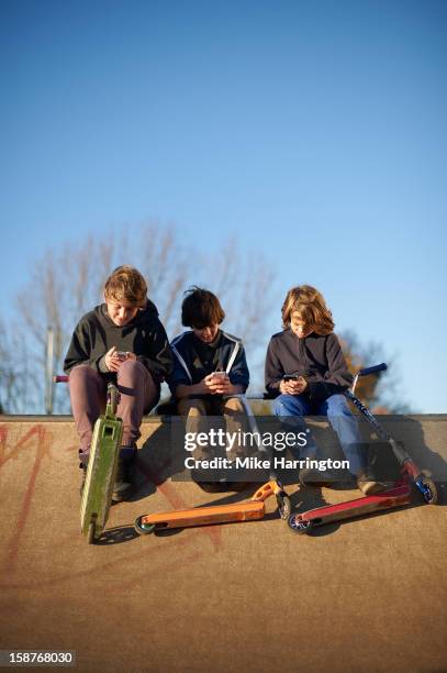 three boys using mobile phones at skate park - 3 teenagers mobile outdoors stockfoto's en -beelden