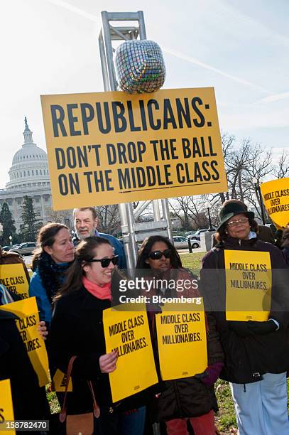 Protesters hold signs that read, "Middle Class Over Millionaires" while standing under a sign that reads, "Republicans: Don't Drop the Ball on the...