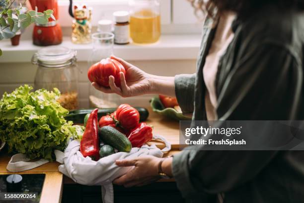 an unrecognizable woman holding a tomato - peper groente stockfoto's en -beelden