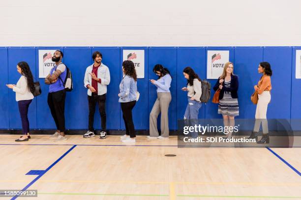 diverse group of voters stand in line waiting to be assigned to a booth - rösta bildbanksfoton och bilder