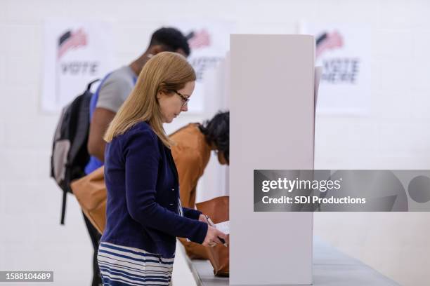 multiracial group fills out ballots at voting booths - bi partisan stock pictures, royalty-free photos & images