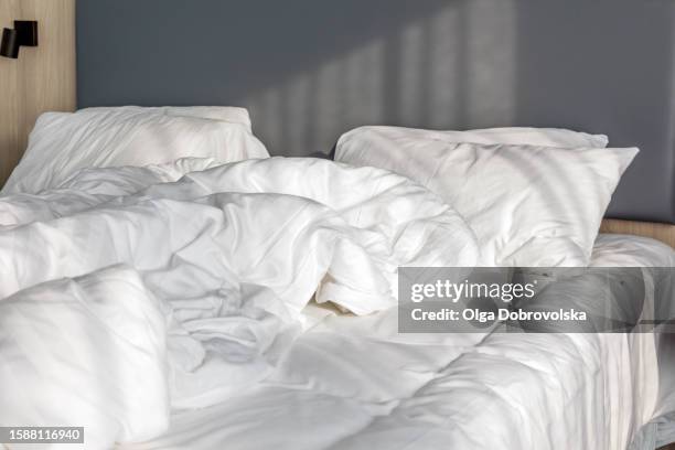 close-up of an unmade bed with a white bed linen and a soft light from a window in the morning - manta-ropa-de-cama fotografías e imágenes de stock