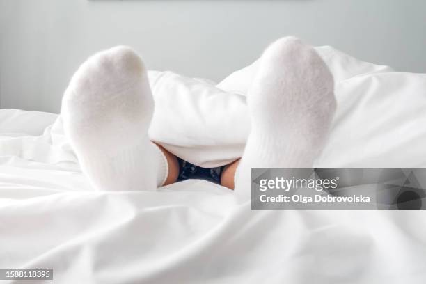 close-up of boy's feet in white socks peeking out from a blanket in a bed - sole of foot stock pictures, royalty-free photos & images